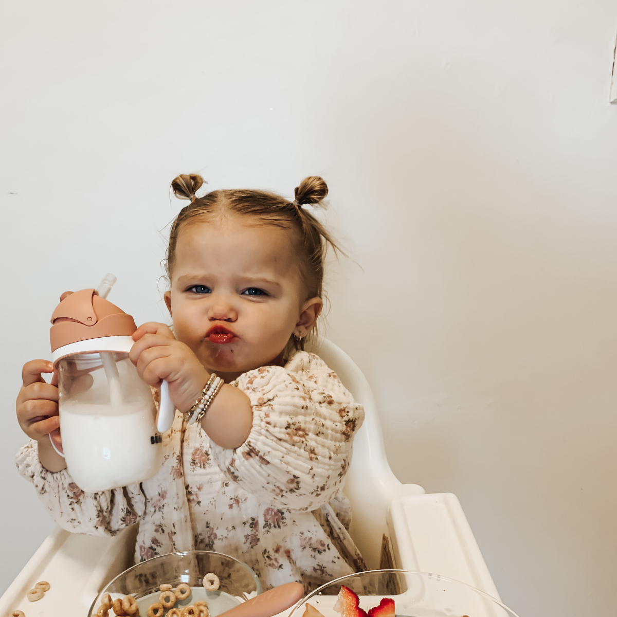 toddler holding pink beaba sippy cup, pursing her lips